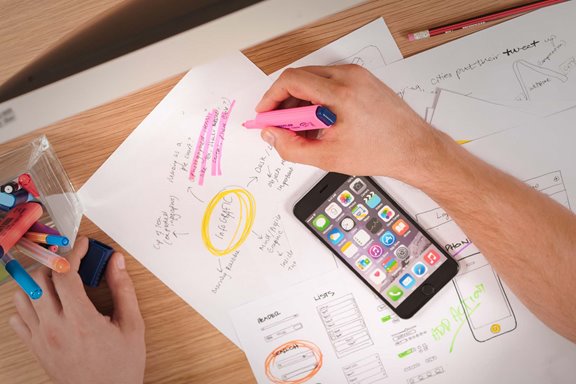 Someone using pens and highlighters to map out strategic planning on paper with their phone next to them