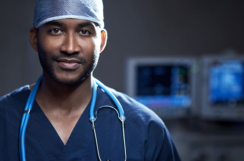 portrait of a doctor in dark blue scrubs with computer screens in the background