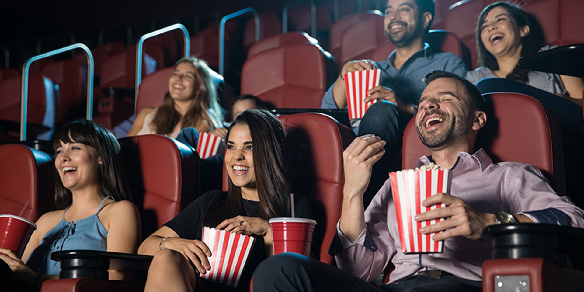 Movie goers eating popcorn and laughing at a movie in a theater 