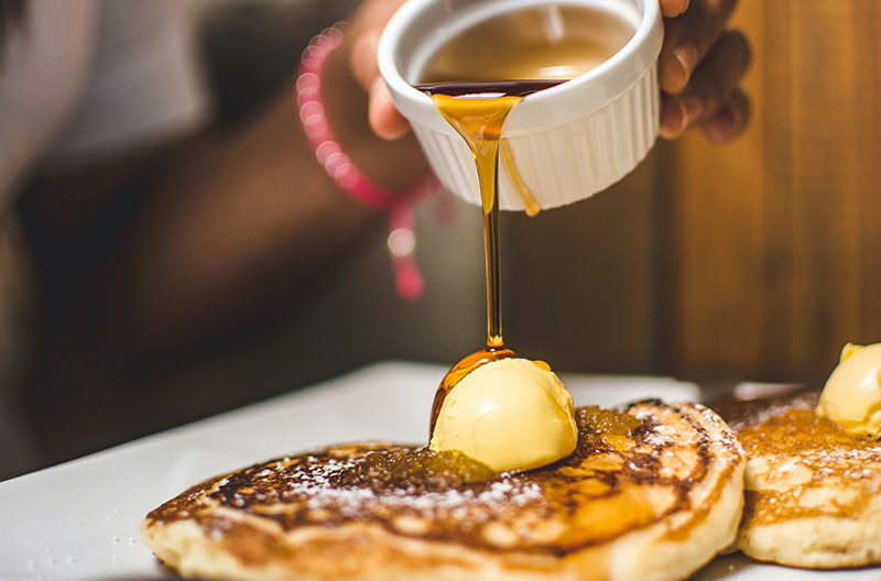 pancakes with a large pat of butterwith syrup pouring over them