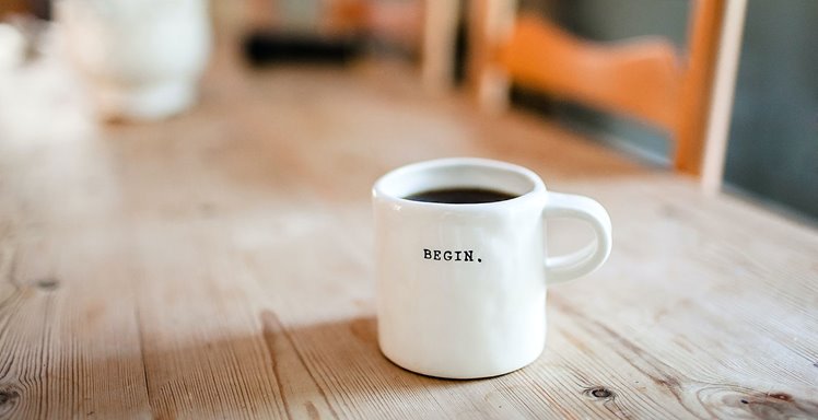 Coffee mug that reads "Begin." on a desk.