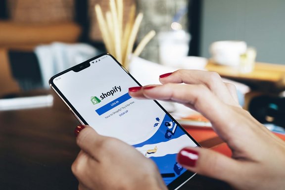 A person holding a phone with the Shopify login screen on it and about to press the button to log in