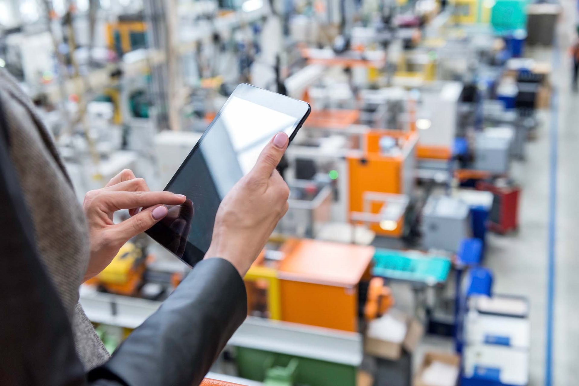 A manufacturing worker looking over a factory floor with a tablet taking Ecommerce inventory. 