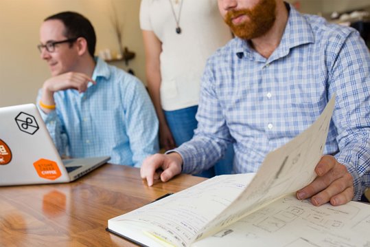 Two Lightburn employees sitting next to each other and one is looking in a notebook full of UX wireframe sketches