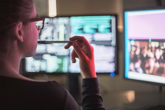 Looking over the shoulder of a web developer monitoring a website on multiple monitors