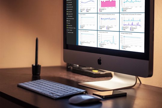 An iMac on a desk in a dimly lit room with a dashboard interface on the screen