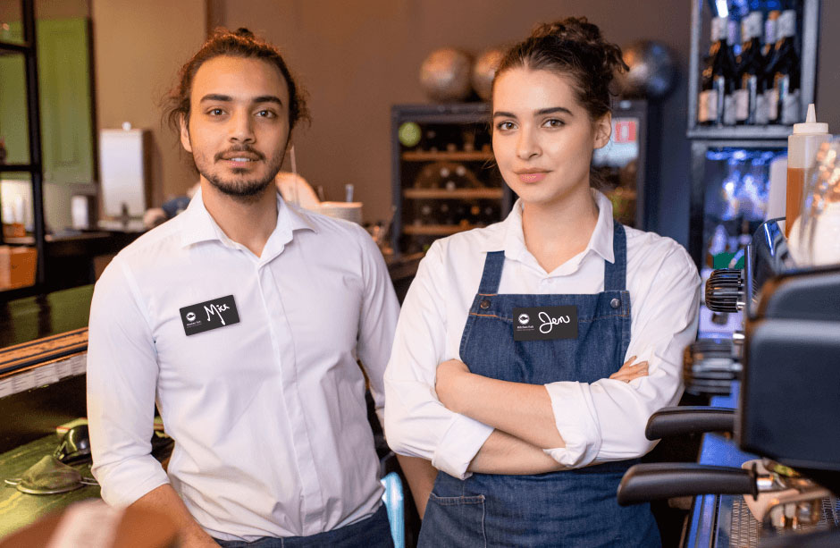 two employees, one with apron, wear name badges that were purchased via ecommerce